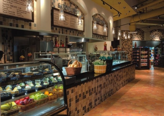 A deli counter with a bakery case, arched signs, and overhead lighting. 