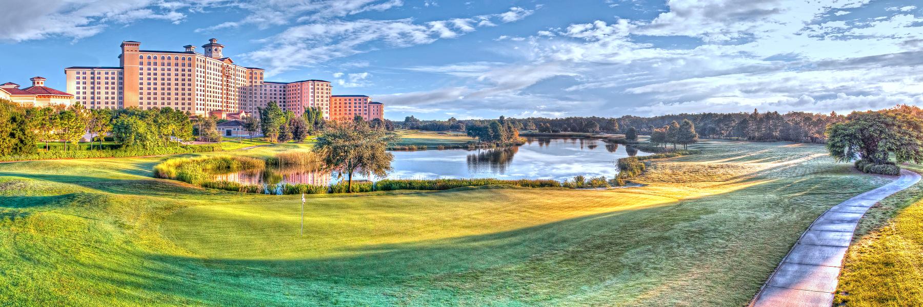 A wide shot of a golf course with a lake and towering hotel in the distance. Pack for a convention at Rosen Shingle Creek.
