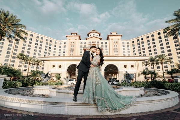 8 Questions to Ask When Choosing a Wedding Venue 6 A bride and groom stand on the edge of a large circular fountain embracing with the front entrance of Rosen Shingle Creek in the background.
