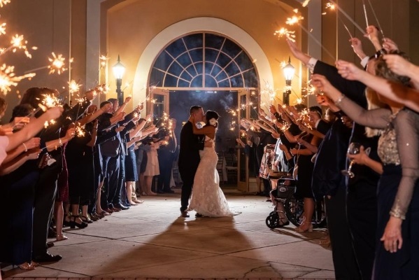 8 Questions to Ask When Choosing a Wedding Venue 4 A bride and groom kiss in an outdoor pathway at night in front of an arched doorway and surrounded by guests holding lit sparklers.