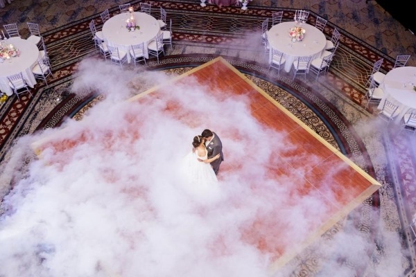8 Questions to Ask When Choosing a Wedding Venue 9 An aerial shot of a bride and groom in the middle of a dance floor dancing surrounded by fog and round tables with white linens.