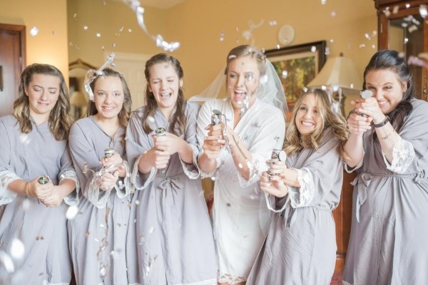 8 Questions to Ask When Choosing a Wedding Venue 3 Five women in gray bathrobes and a bride pop confetti cannons, smiling.