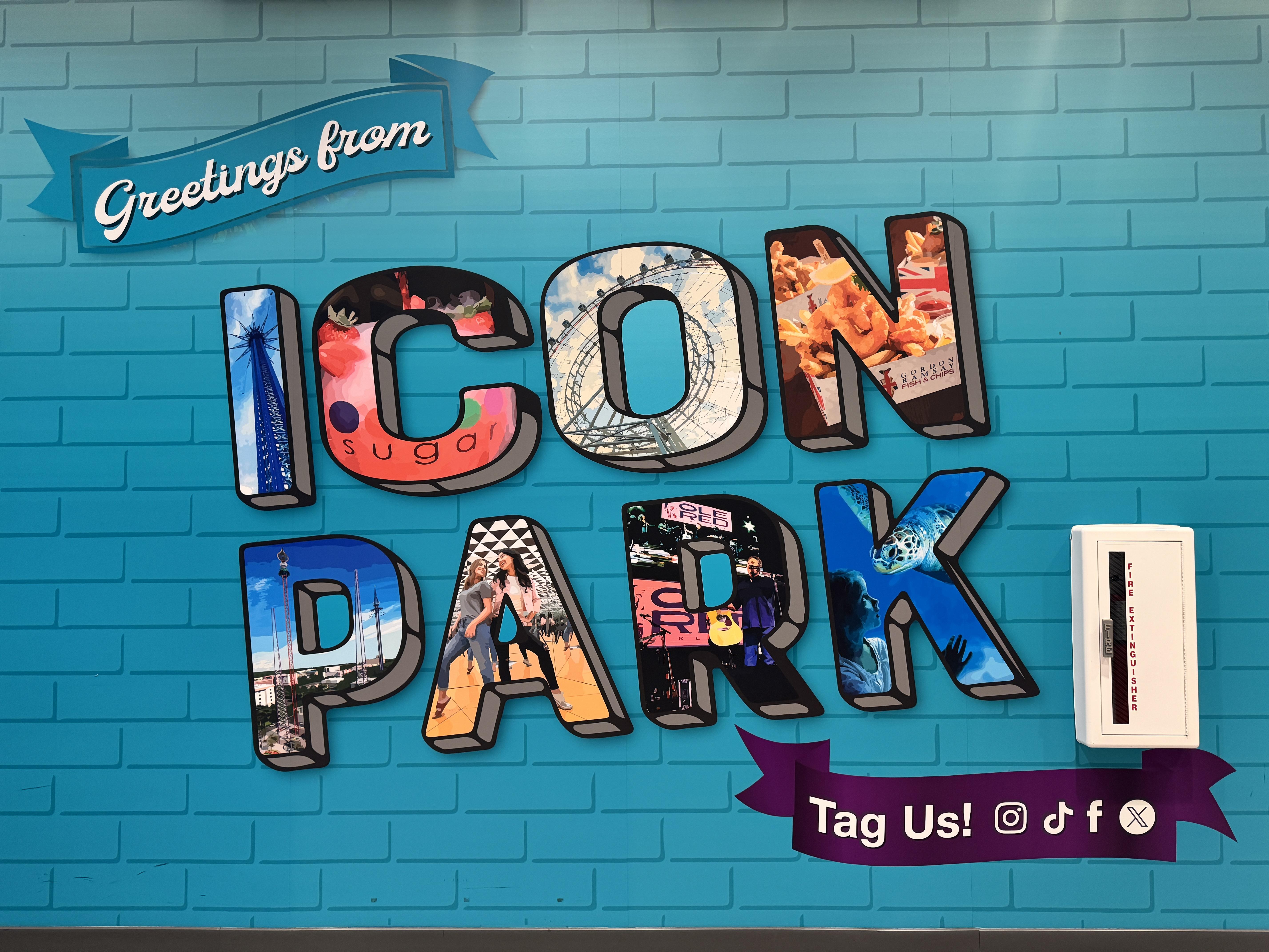 A colorful sign on a blue brick wall that reads "Greetings from ICON Park," with each letter filled with images of attractions and experiences within the park.