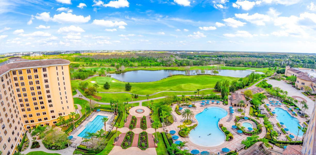 A Perfect Spa Day at Rosen Shingle Creek: What to Expect 1 An aerial shot of four large swimming pools, a lake, golf course, and the side of a tall hotel building.
