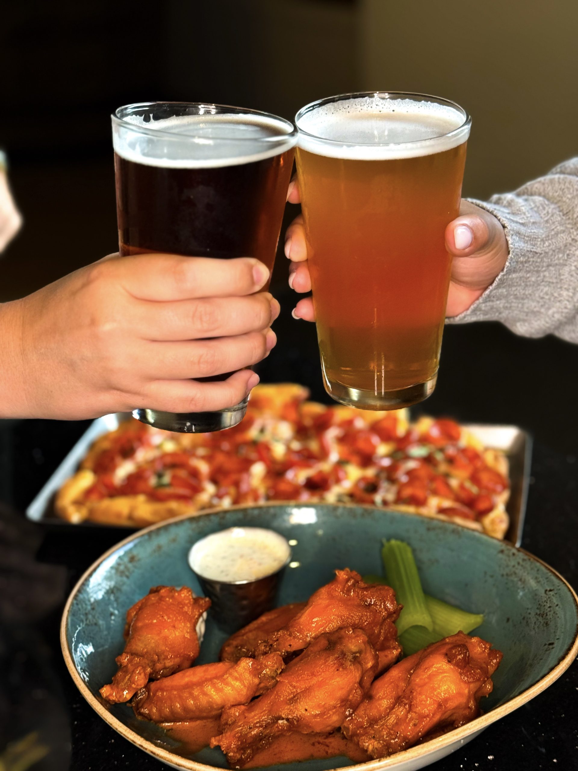 The Restaurants at Rosen Shingle Creek: A Different Dinner Every Night 19 Hands toast with pint glasses of beer over dishes of buffalo wings and pizza at Headwaters.