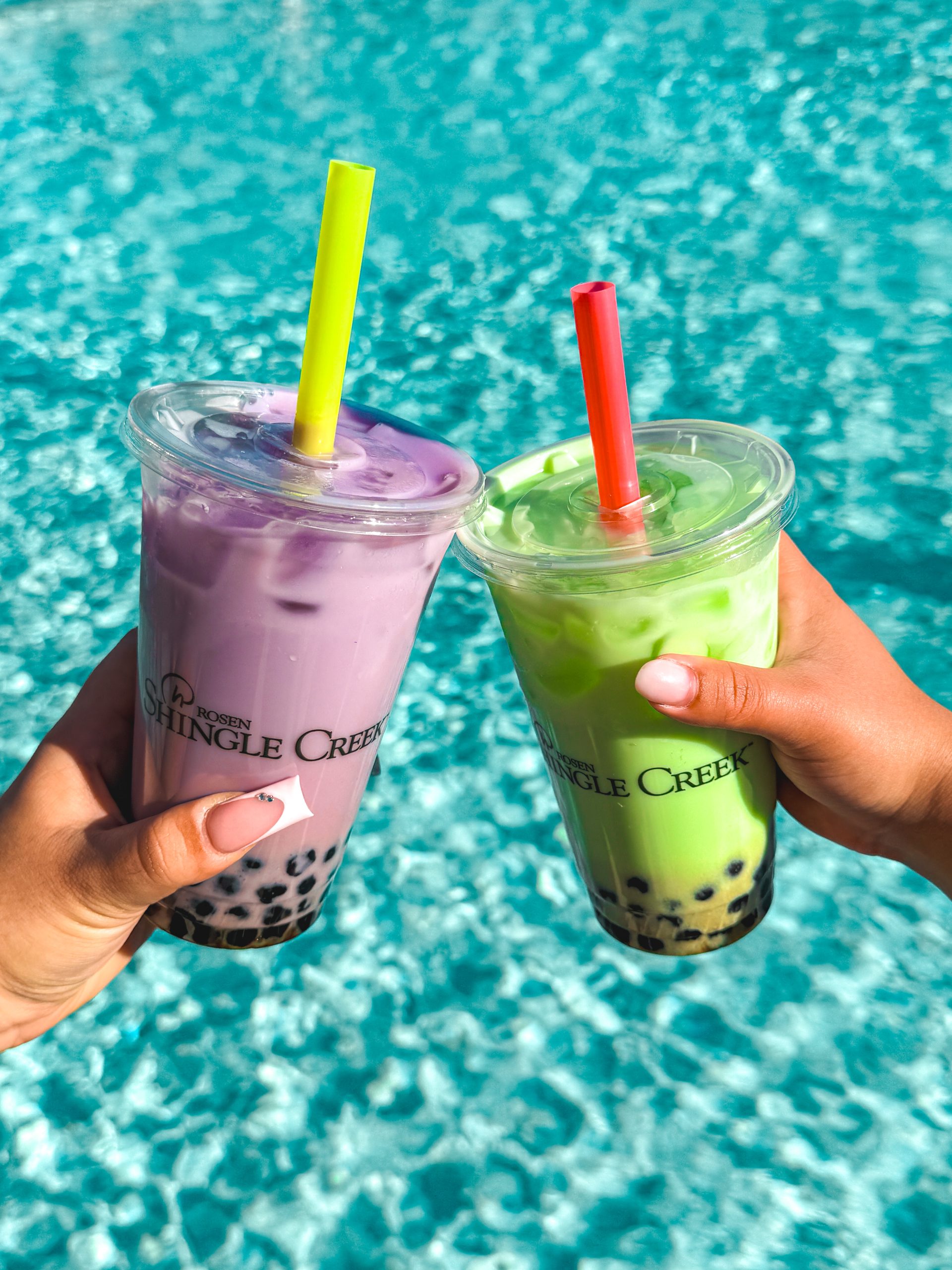 The Restaurants at Rosen Shingle Creek: A Different Dinner Every Night 18 Two hands hold purple and light green boba drinks against the clear blue pool water.