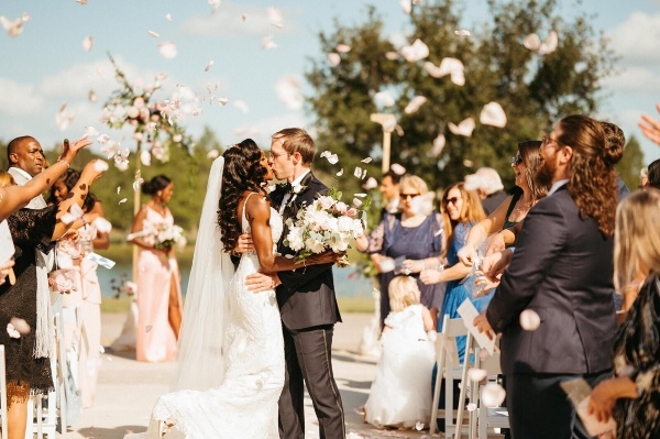 8 Questions to Ask When Choosing a Wedding Venue 1 Outside in front of a lake and trees, a bride and groom pause to share a kiss in the aisle surrounded by people throwing white rose petals. Rosen Shingle Creek is a beautiful wedding venue in Orlando.