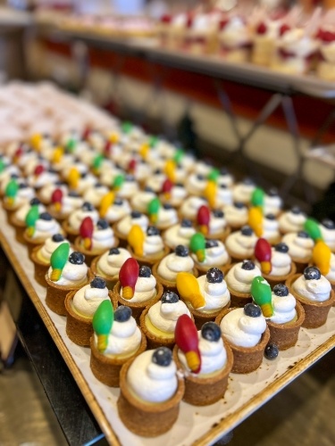 A tray of mini tartlets topped with whipped cream, blueberries, and Christmas light candies. 
