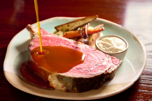 Magical Dining 2026 at A Land Remembered in Orlando 3 Rich au jus sauce being poured onto a large cut of prime rib on a plate for Magical Dining at A Land Remembered.