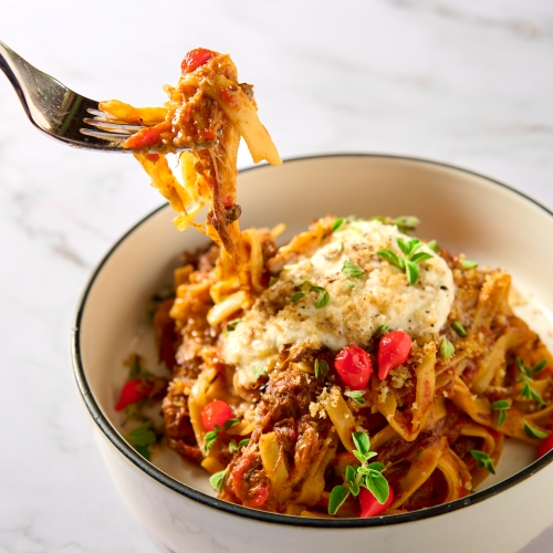 A dish of pasta with colorful peppers, cheese, and garnished with herbs. This is the oxtail fettucine featured in the Magical Dining menu at Cala Bella. 