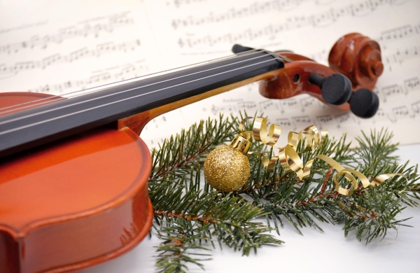 A violin laying on a wooden table next to pine decorations with gold accents.