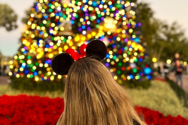 The Ultimate Guide to Orlando Holiday Events 2 A woman in Minnie ears faces away from the camera, looking at a sparkling Christmas tree.