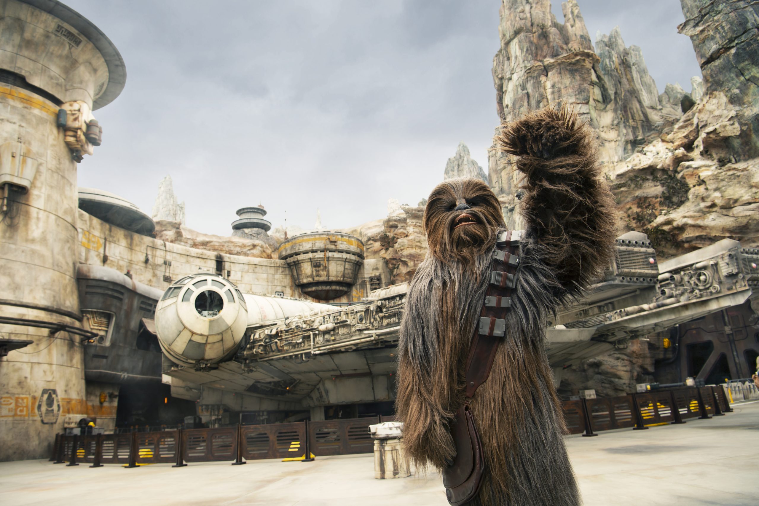 Celebrate Dad: 7 Thoughtful Father’s Day Gift Ideas 6 A large furry costumed character, Chewbacca, waves to the camera standing in a rocky space-inspired theme park.