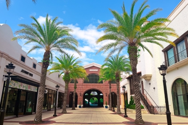 The Ultimate Guide to Orlando Holiday Events 8 Storefronts and an arched brick entryway flanked by Palm Trees at Disney Springs.
