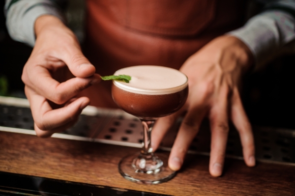 A close-up on hands placing a garnish on an espresso martini.