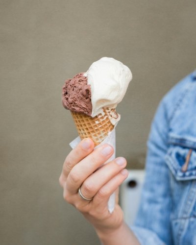 Keep Your Cool at Orlando’s 10 Best Ice Cream Parlors 8 A close-up of a woman in a denim jacket holding a waffle cone with a scoop of chocolate and vanilla ice cream.