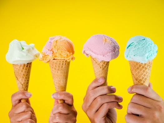 Keep Your Cool at Orlando’s 10 Best Ice Cream Parlors 1 Four hands holding ice cream cones with different colors of scooped ice cream against a bright yellow backdrop.