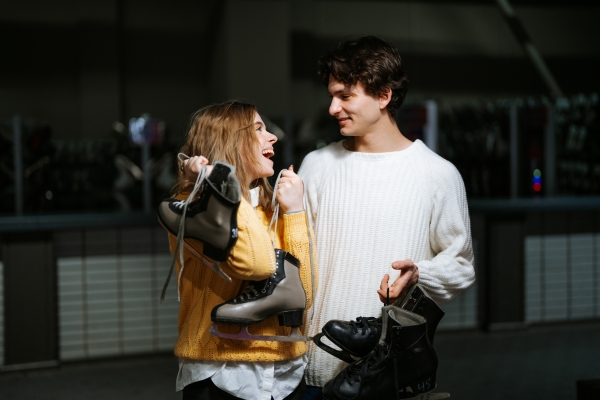 A young man and woman holding ice skates smile at one another on a romantic holiday date night.