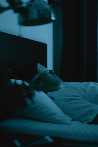 A man in a sleep mask sleeps on his back in bed in the dark.