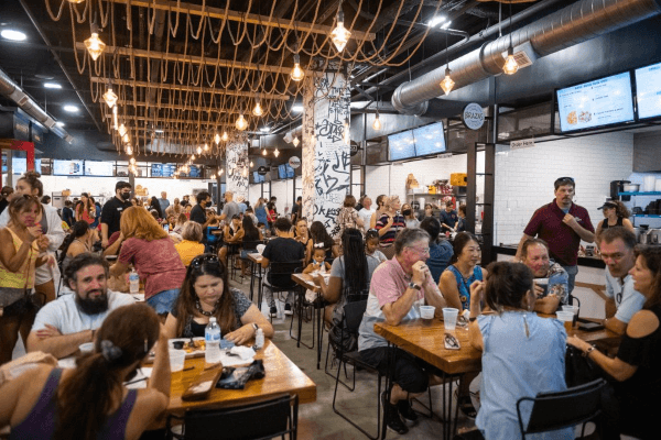 Eats for Everyone: 6 Must-Try Food Halls in Orlando 1 A large room full of people seated and dining at wooden tables.