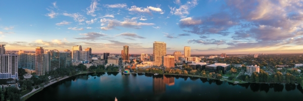 A panoramic shot of downtown Orlando at twilight with tall building surrounding a serene lake.