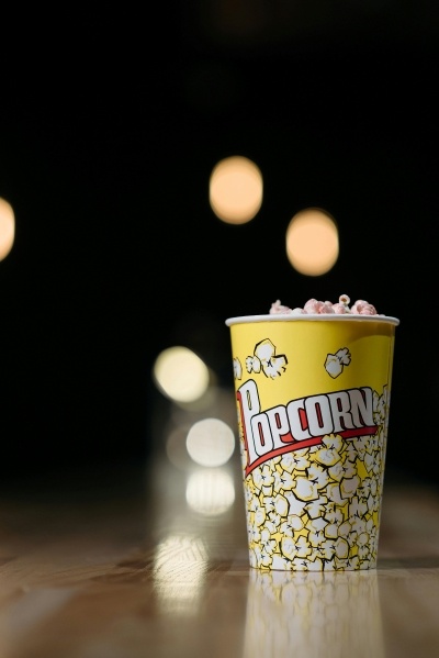 Have a Reel Good Time at the 2025 Florida Film Festival 2 A yellow bucket of popcorn that says “popcorn” on a wooden surface against a dark background. Enjoy popcorn and other food when you attend a Florida Film Festival movie at The Enzian.