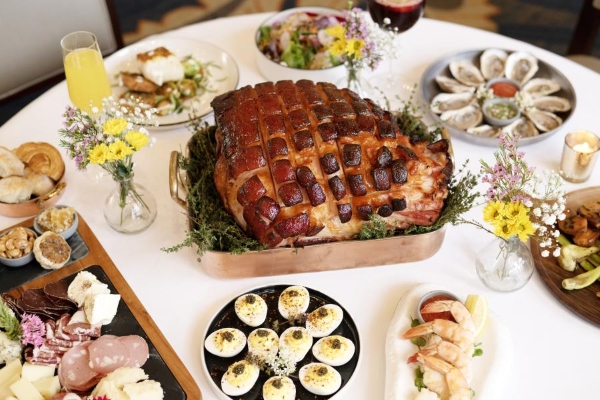 A beautiful table spread with a roast ham, deviled eggs, charcuterie, yellow flowers, and mimosas.