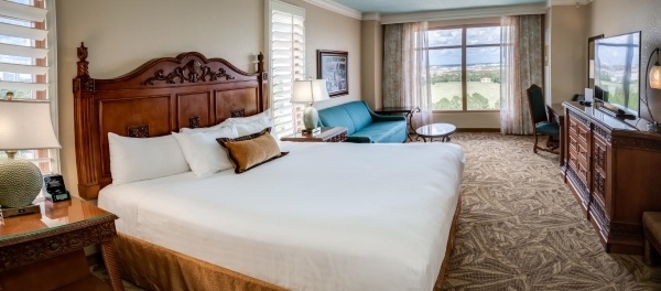 A wide shot of a room with a bed and large wooden headboard, a blue sofa, and a window overlooking a golf course.
