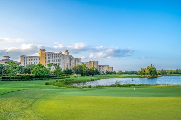 A sprawling green lawn surrounding a lake with trees and a towering hotel in the distance. Enjoy Father's Day at Rosen Shingle Creek.