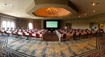 A meeting room set up with long rows of tables and chairs beneath a Chandelier