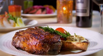 A plated steak with a sprig of rosemary, a bottle of wine and a lit candle in the background