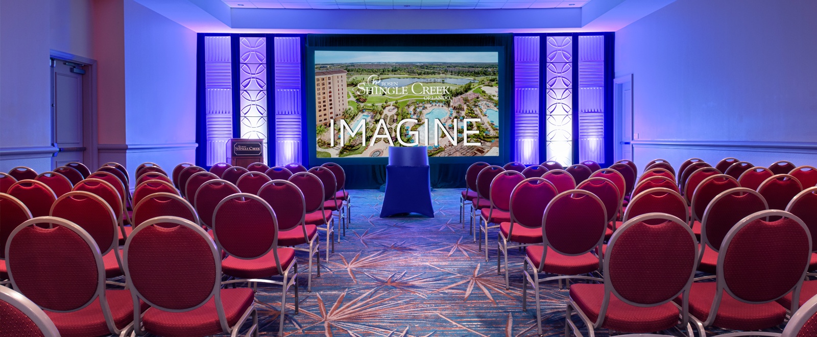 Rows of red chairs facing a screen with an image of Rosen Shingle Creek and the word "Imagine"