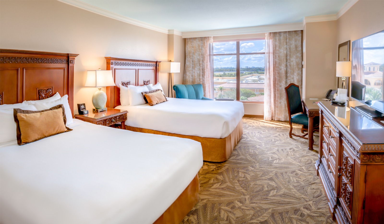 Two queen beds with wooden headboards and white linens in a room with a window overlooking the golf course