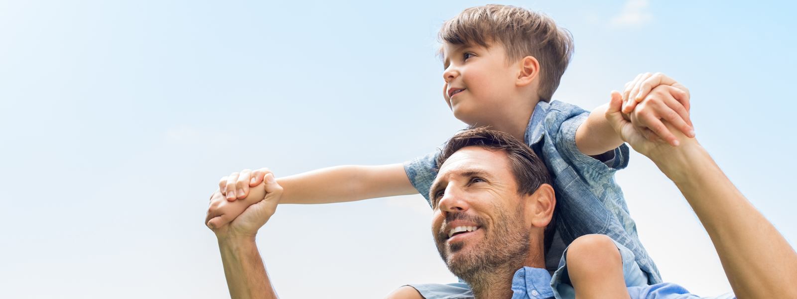 A man holds the hands of a boy sitting on his shoulders