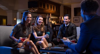 Four people with drinks in hand sitting in a lounge area of a dimly lit bar