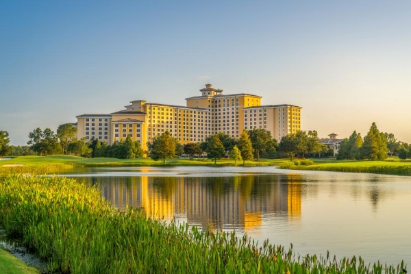 The exterior of Rosen Shingle Creek hotel in Orlando, surrounded by a beautiful lake and lush greenery.