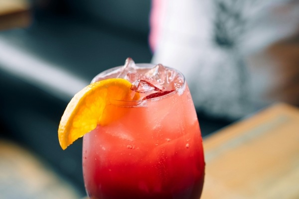 A close-up of a glass with red sangria, garnished with an orange wedge.