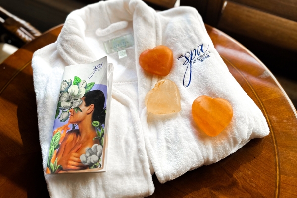 A white robe with the Spa at Shingle Creek embroidered, resting beneath a spa menu and pink Himalayan salt stones.