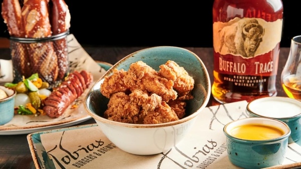 A bowl of fried chicken tenders next to a display of soft pretzel sticks and a bottle of whisky.