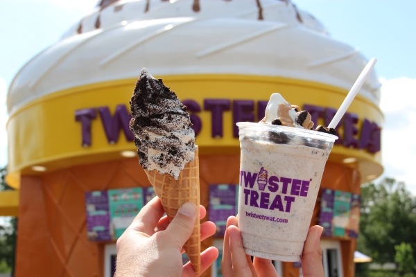 Keep Your Cool at Orlando’s 10 Best Ice Cream Parlors 4 Two hands, one holding an ice cream cone of cookie-dusted soft-serve and the other holding soft-serve in a Twistee Treat cup in front of a large Twistee Treat building.