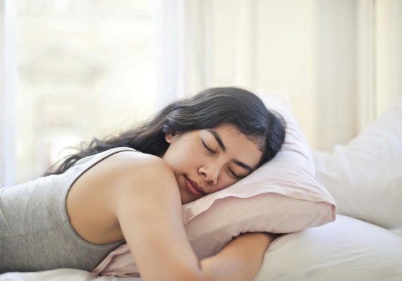 A woman holds a pillow as she sleeps on her stomach. 