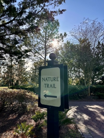 Outdoor sign reading "nature trail" with an arrow pointing to a path of trees along an Orlando hiking trail. 