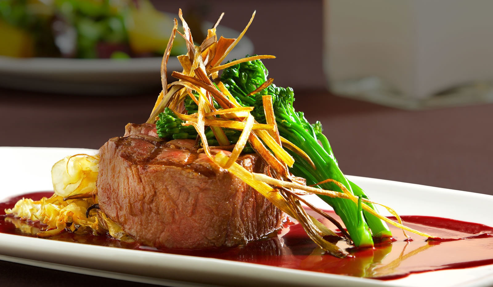 A plated steak with a brown sauce, crispy potatoes, and green broccolini