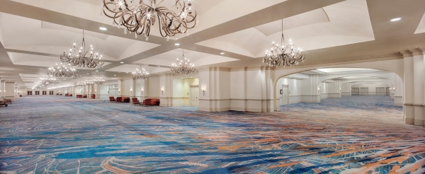 An expansive hallway with blue patterned carpet, large arched entryways, and dozens of hanging wrought iron chandeliers. 