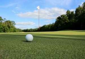 A golf ball sitting on the putting green of a golf course right by a cup.