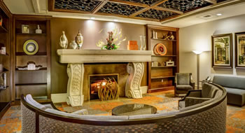 A curved brown sofa in front of a lit white stone fireplace flanked by wooden bookshelves.