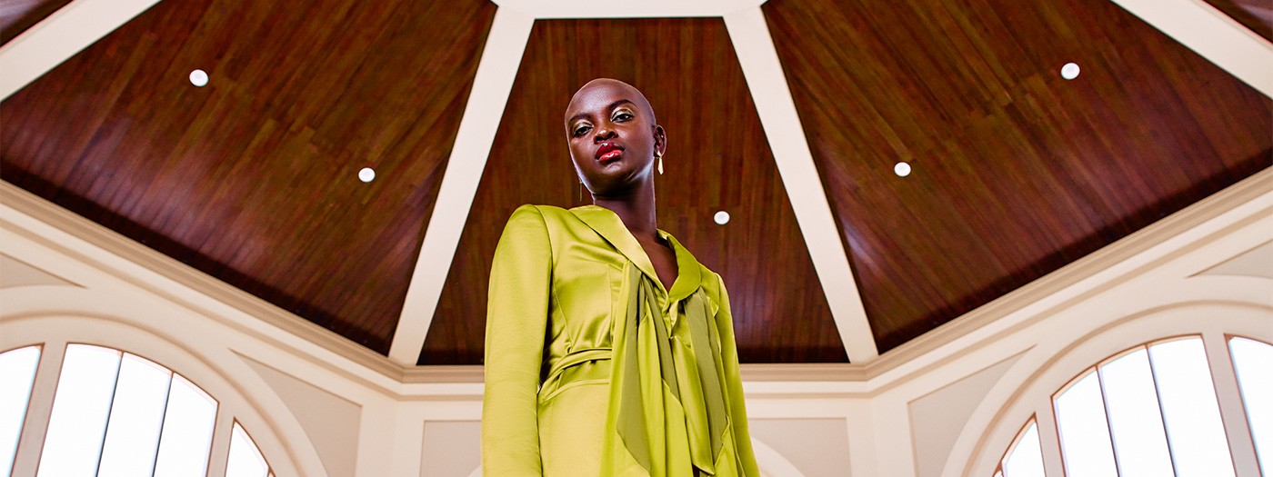 A woman in a lime green outfit stands beneath a pergola ceiling with wood panels and white beams