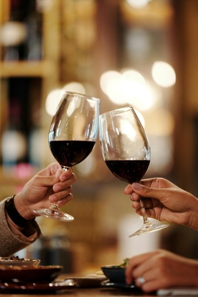 Hands toasting two glasses of red wine in a dimly lit restaurant. 