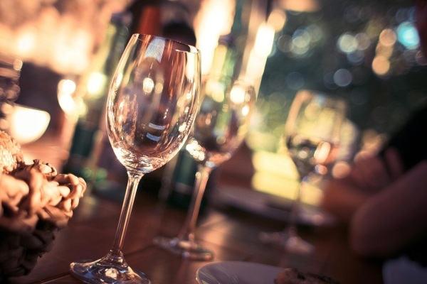 Two glasses of wine in the foreground of an out-of-focus shot of a dimly lit bar.