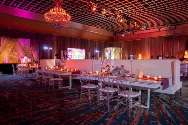 A beautiful event setup with booth seating, pink florals, candles, glowing tiered chandeliers, and pink and red lighting.